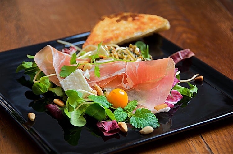 Parmaskinka, fårost, pesto och pinjenötter på salladsbädd